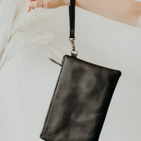 Black leather convertible handbag worn as a clutch, removable strap
