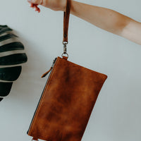 Convertible crossbody brown leather handbag, worn as a clutch bag